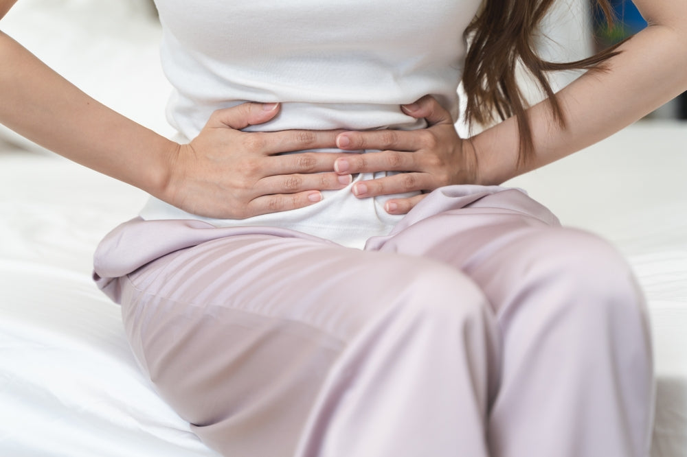 Frau sitzend auf dem Bett die Hände vor dem Bauch verkrampfend